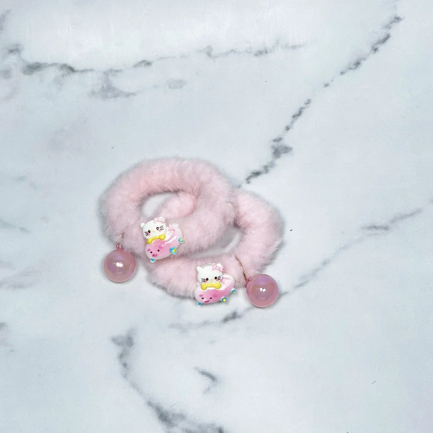 Pink kids furry hair ties with cute cat and donut charms on a marble background