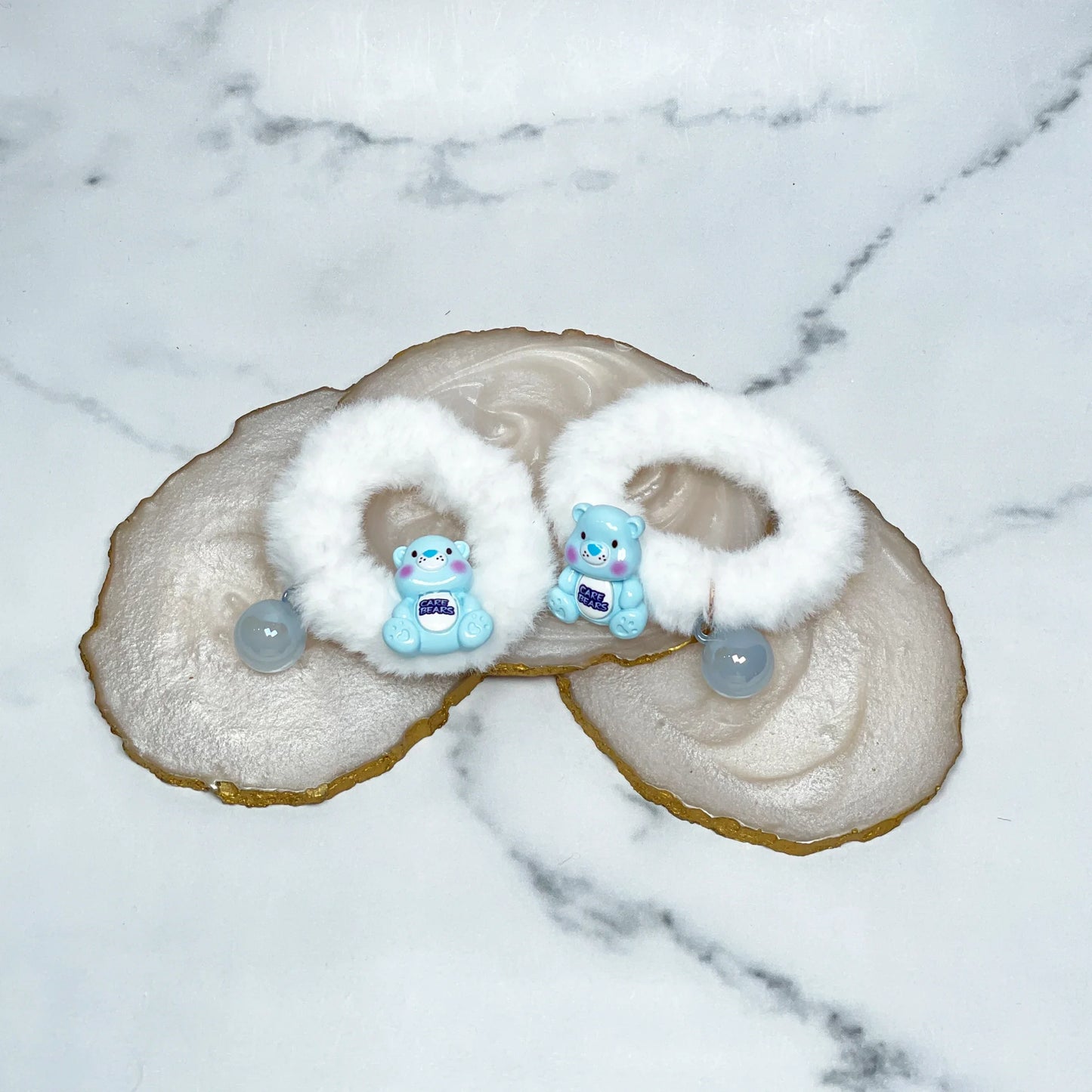 White kids furry hair ties with blue bear charms and beads on marble background