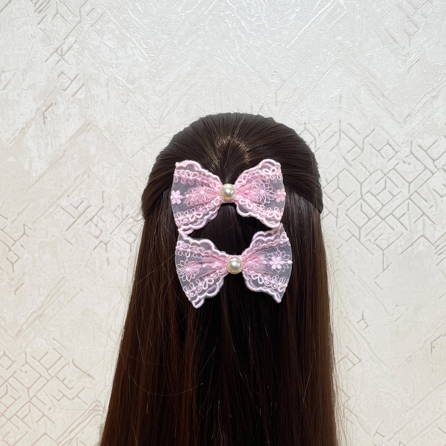 Pink lacy alligator bow clips with pearl centers clipped in long dark brown hair