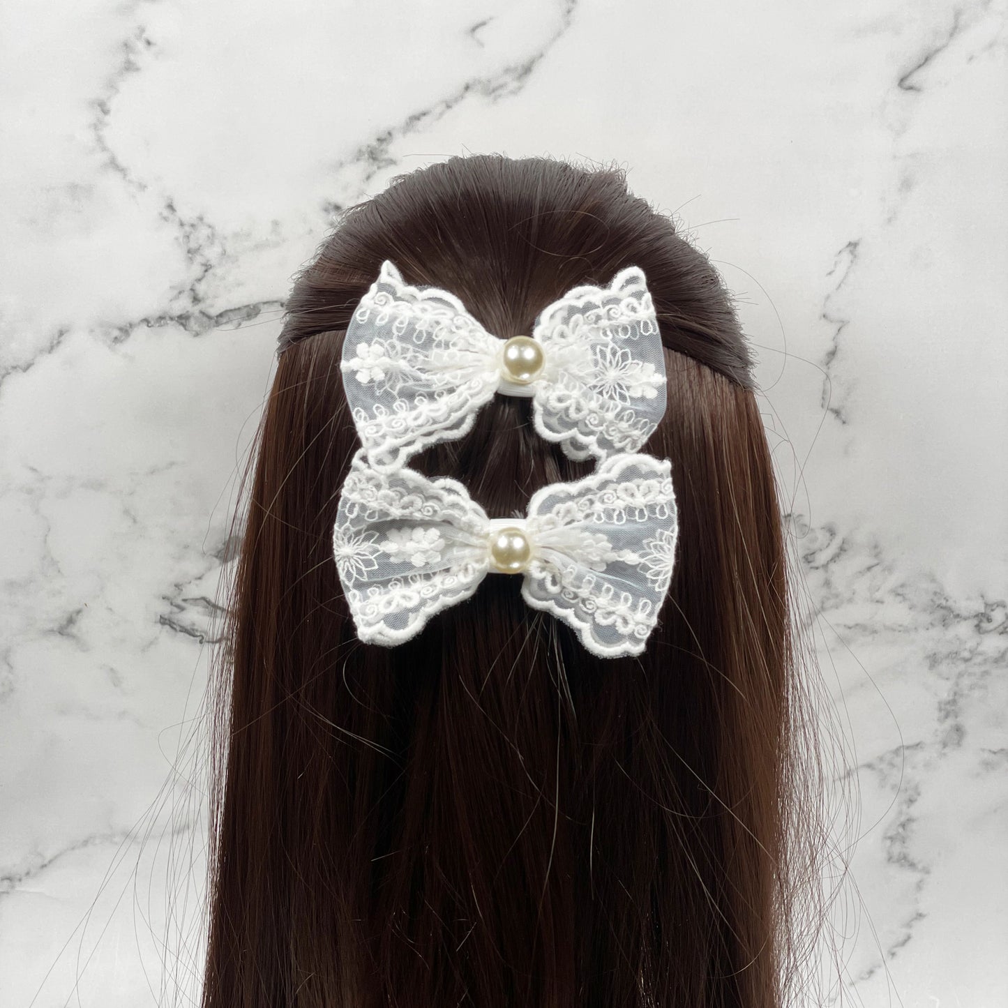 White lacy alligator bow clips with pearl center worn on dark brown hair with marble background