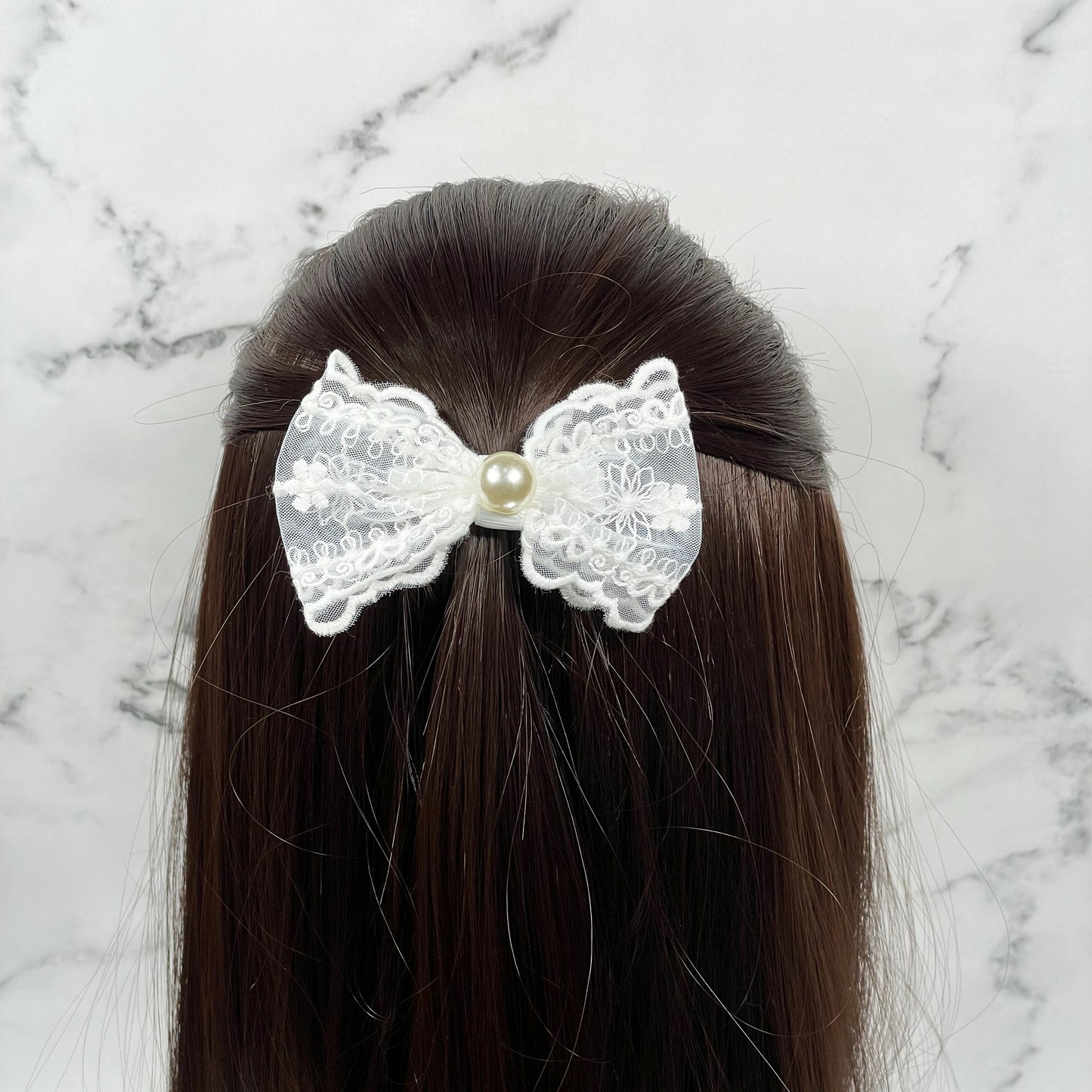 White lacy alligator bow clips with pearl center worn on dark brown hair against marble background