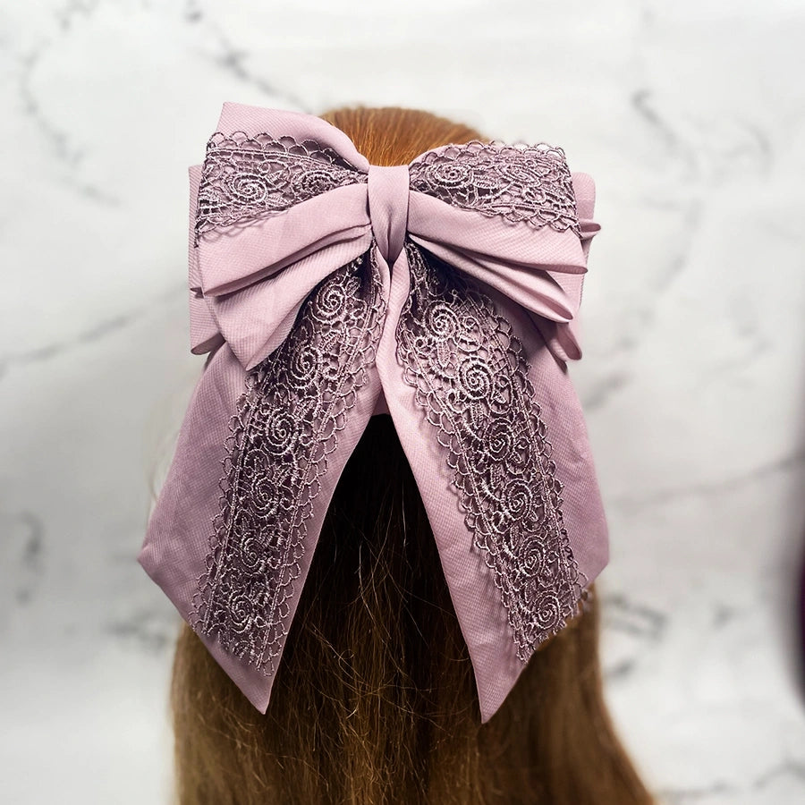 Pink lacy hair bow clip with intricate lace detailing worn on brown hair
