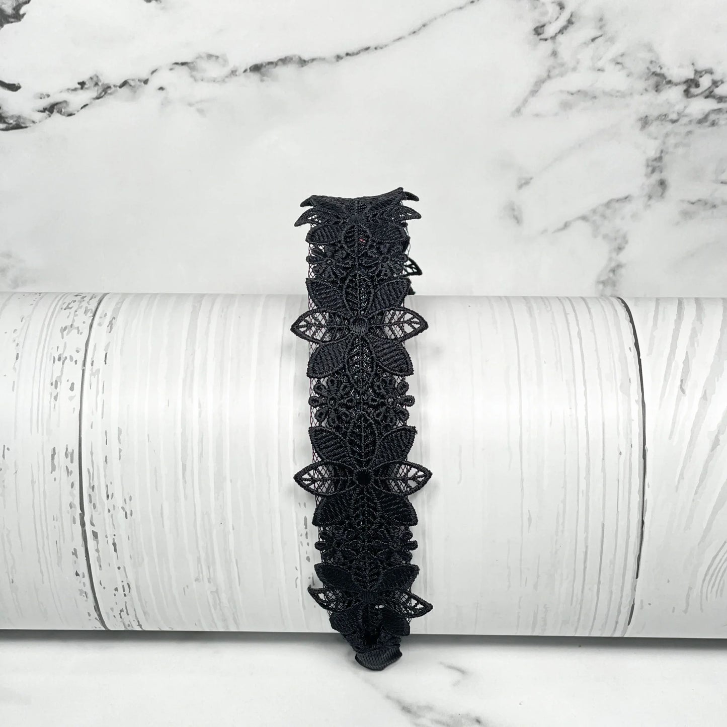 Black medium broad colored hair bands with intricate floral lace design on white wooden background