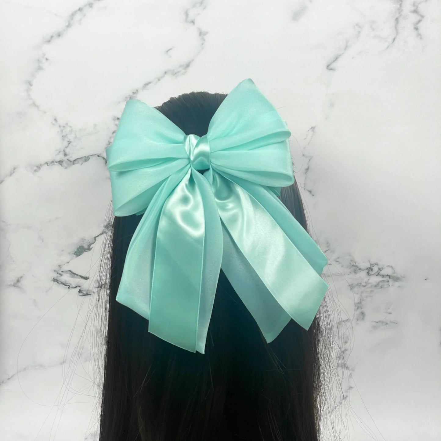Light blue Organza and Satin Bow Clips adorning long dark hair against marble background