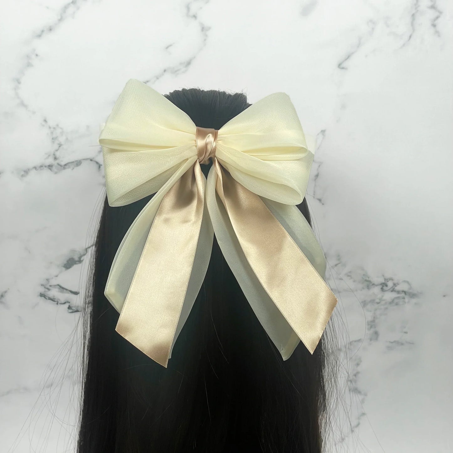 Cream colored Organza and Satin Bow Clips attached to black hair against a marble background