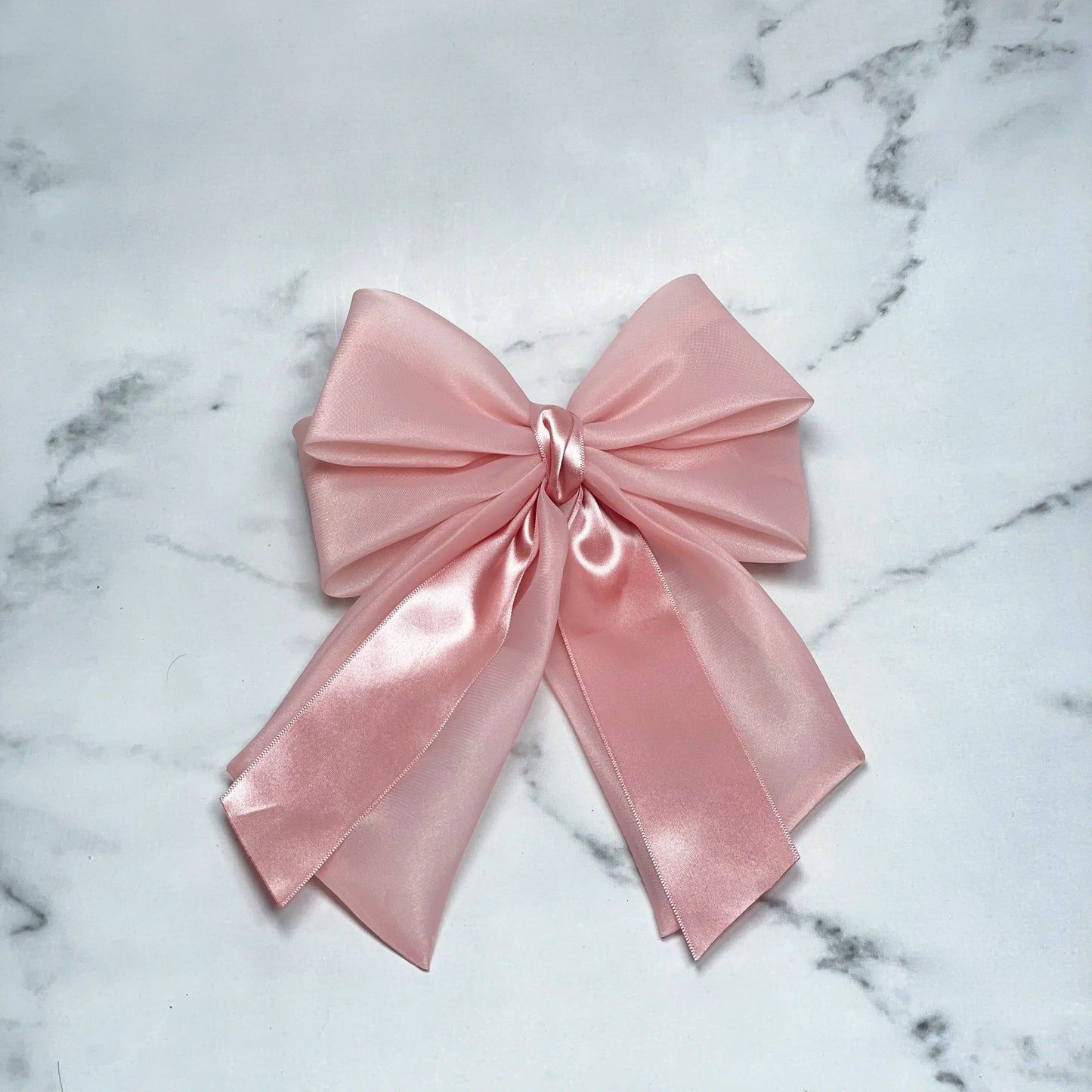 Pink Organza and Satin Bow Clips with a smooth, shiny finish laid on a marble surface