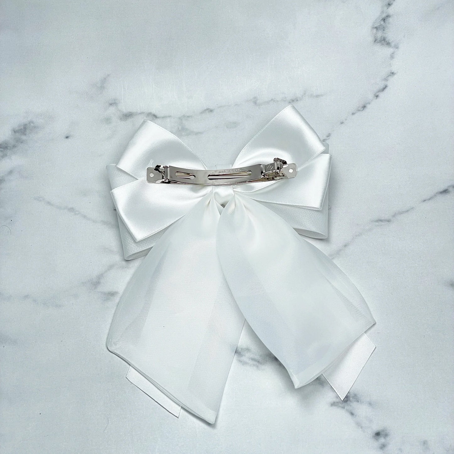 White Organza and Satin Bow Clips with silver metal clasp on marble background