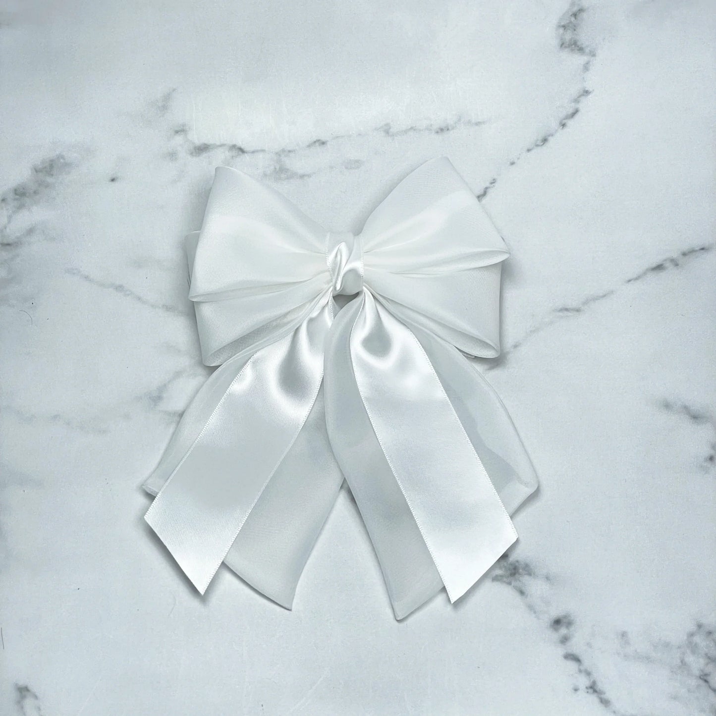White organza and satin bow clips with layered ribbons on a marble background