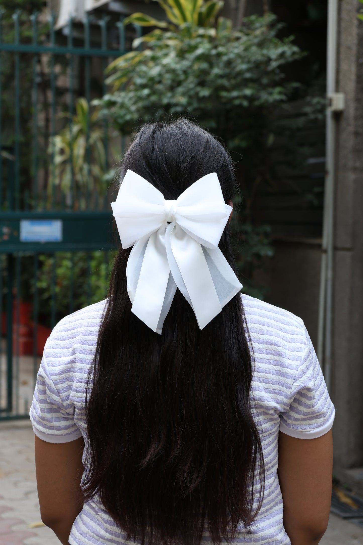 White organza and satin bow clips worn on long dark hair on a woman in a striped shirt outdoors