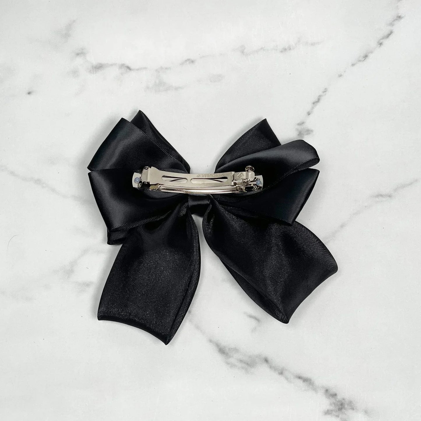 Black organza satin bow hair clips with metal clasp on marble background