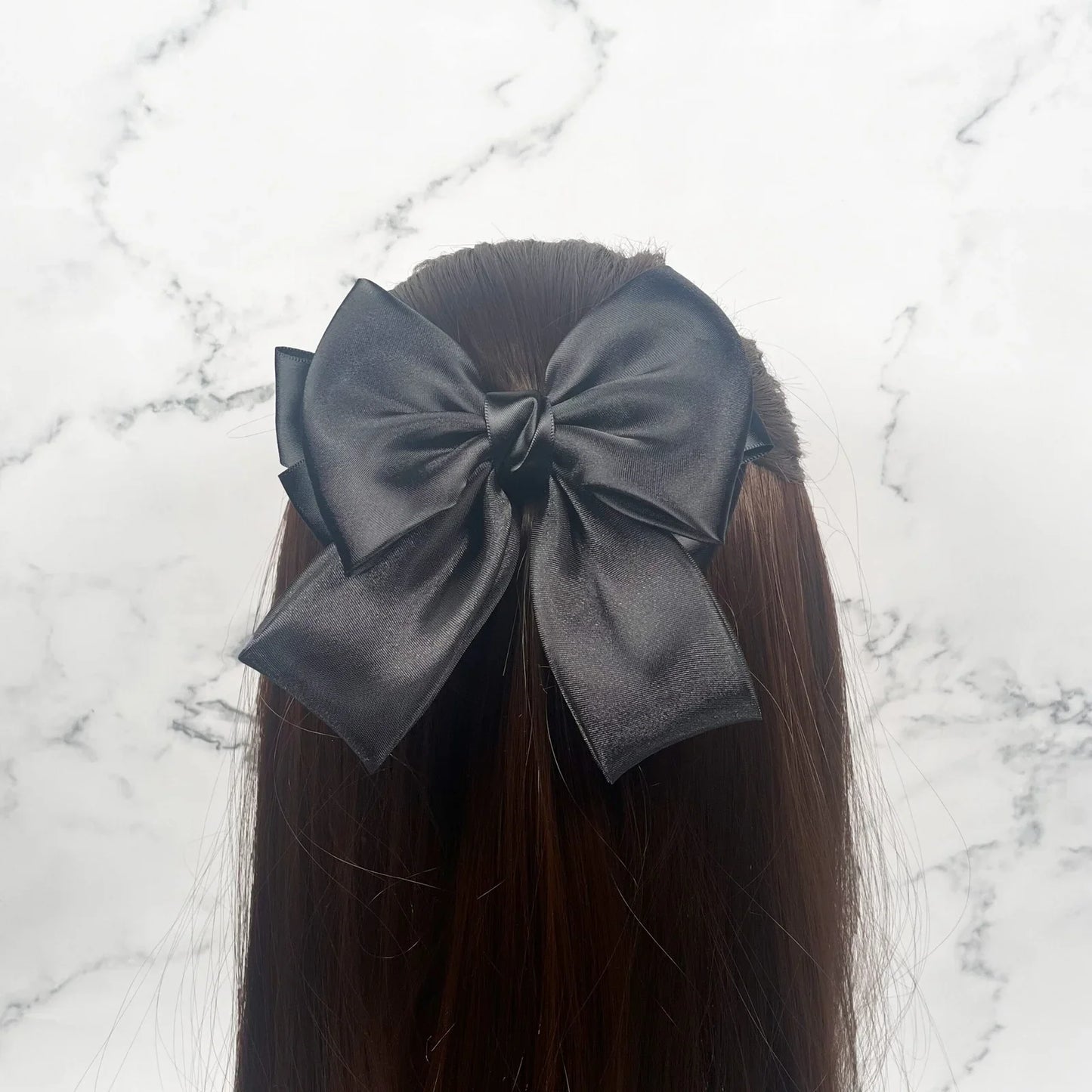 Black organza satin bow hair clips styled on long brown hair against marble background