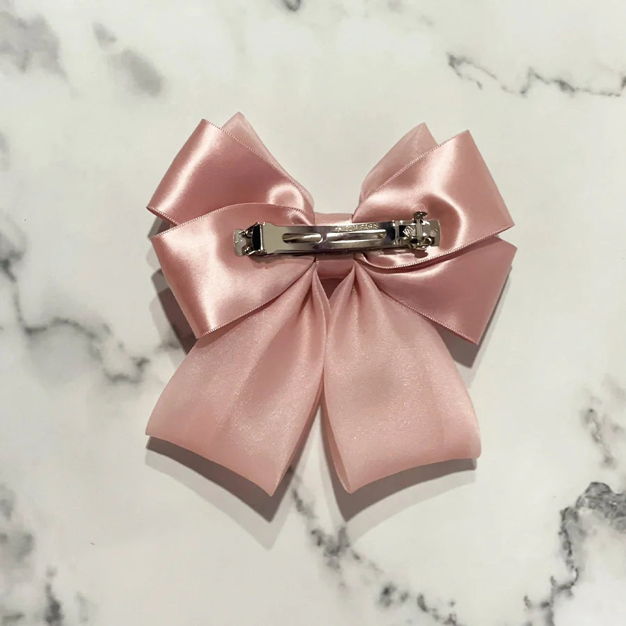 Pink organza satin bow hair clips with metal clip back on a white marble surface