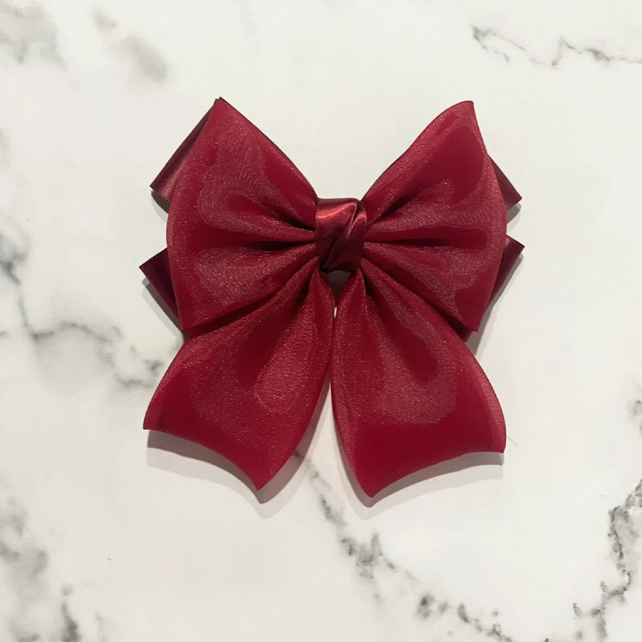 Red organza satin bow hair clips with layered design on white marble background