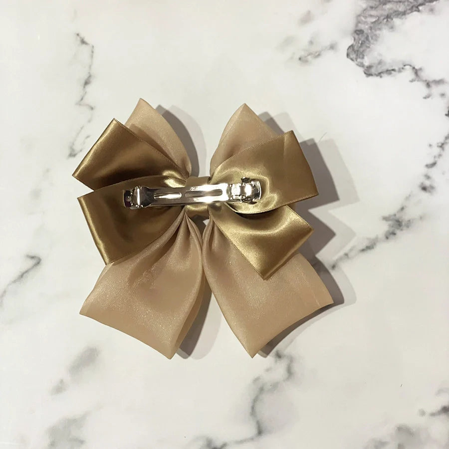 Gold organza satin bow hair clips with metal clasp on marble surface