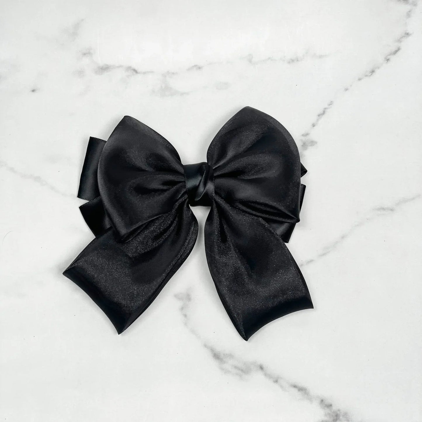 Black organza satin bow hair clips with a smooth shiny finish on a white marble background