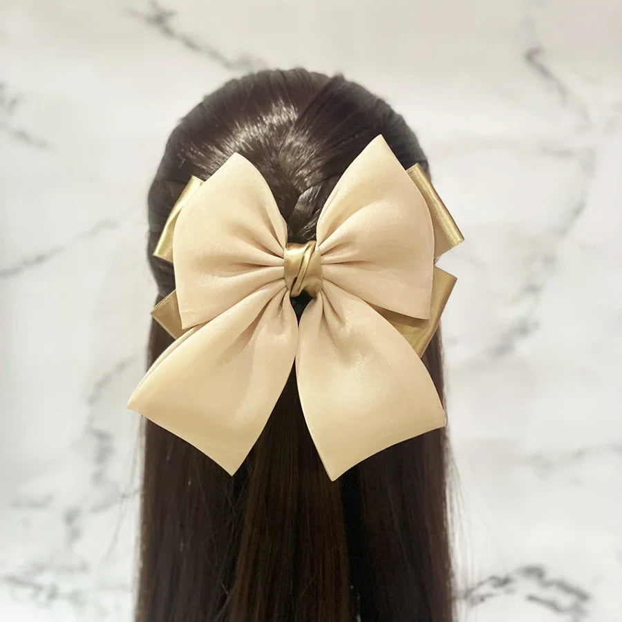 Gold organza satin bow hair clips styled on dark brown hair against a marble background