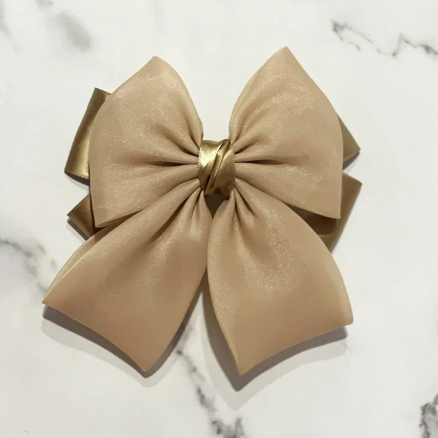 Beige organza satin bow hair clips with a shiny gold knot detail on a marble background