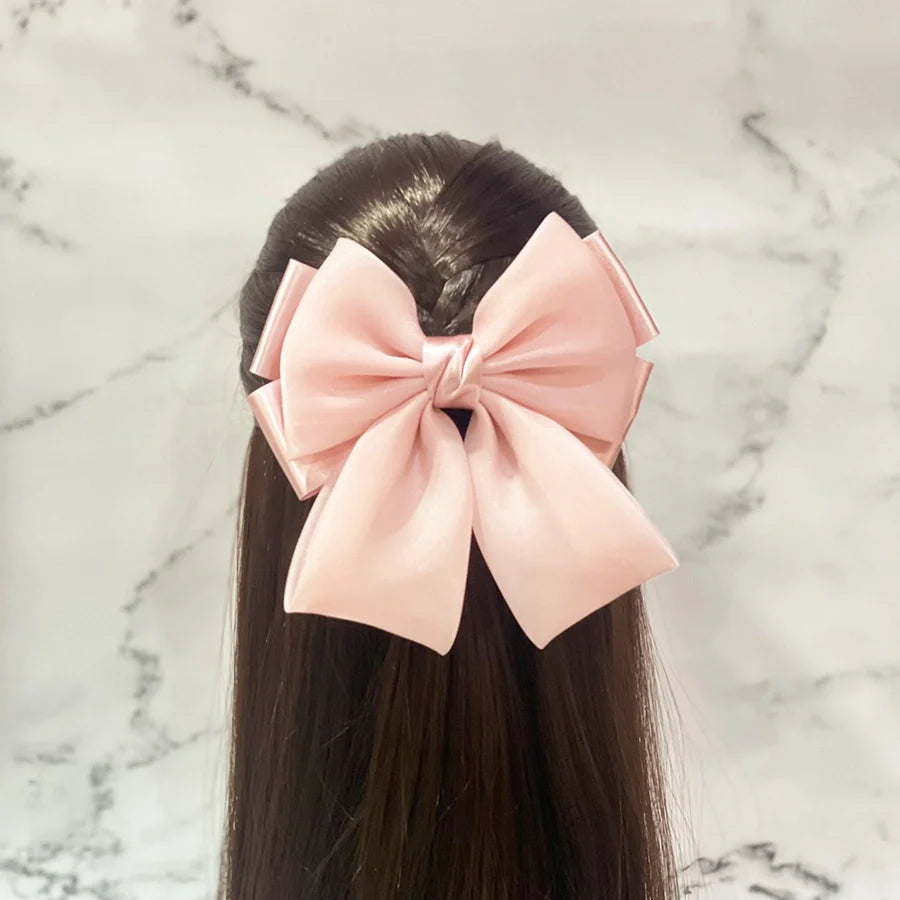 Pink organza satin bow hair clips styled on dark long hair against marble background