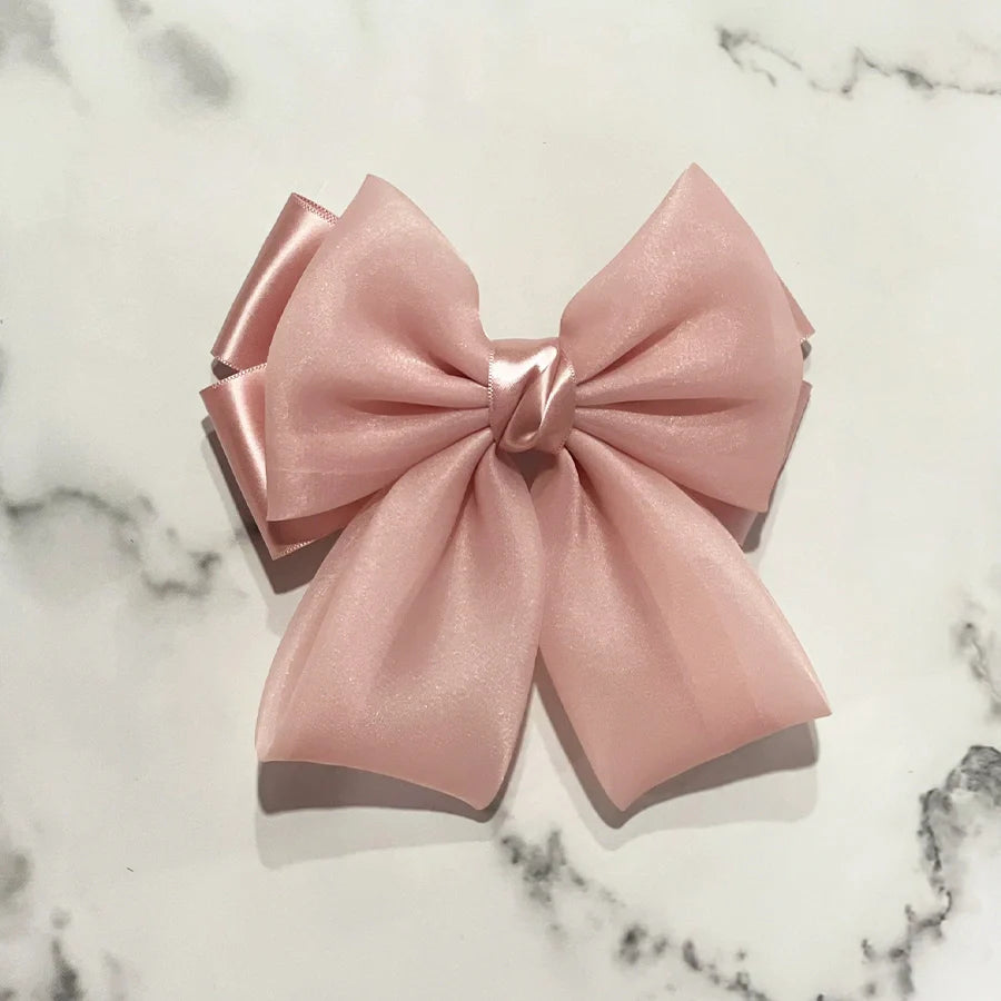 Pink organza satin bow hair clips with layered ribbon design on marble background