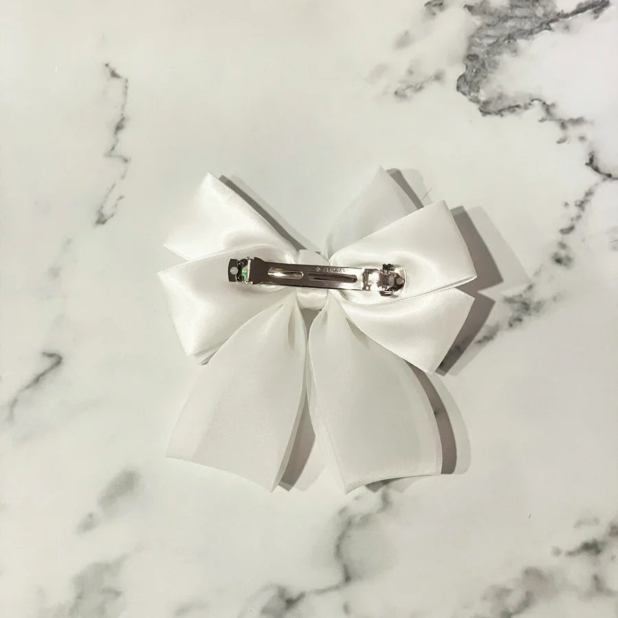 White organza satin bow hair clips with metal clasp on marble background
