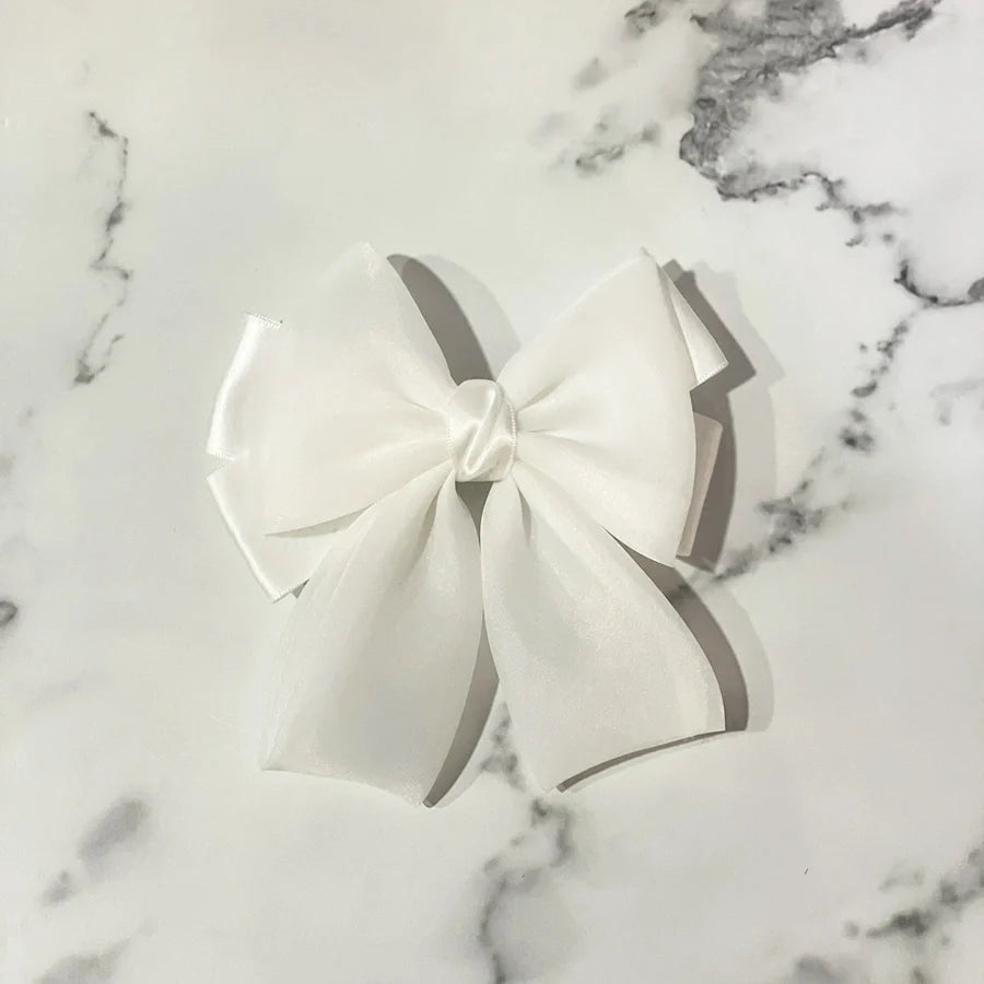 White organza satin bow hair clips displayed on a marble surface by mydevelopmentstor