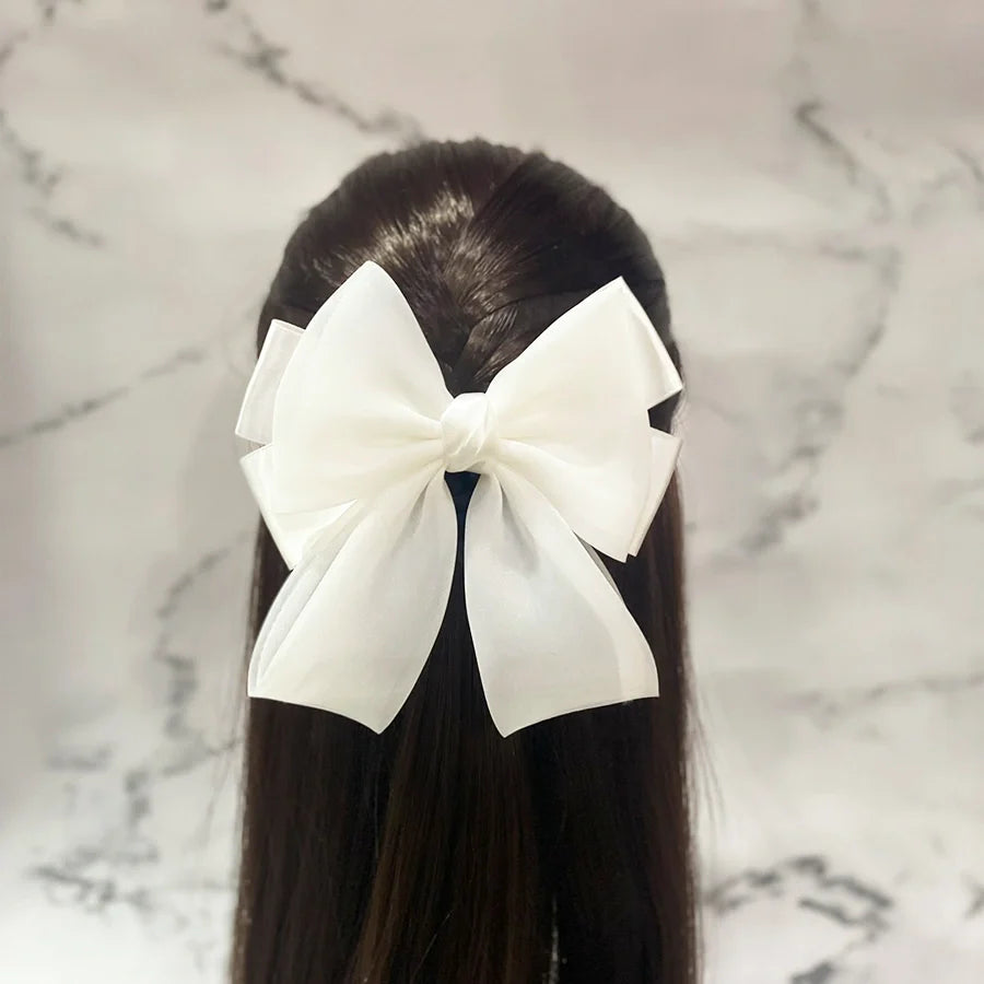 White organza satin bow hair clips styled on long dark hair against marble background