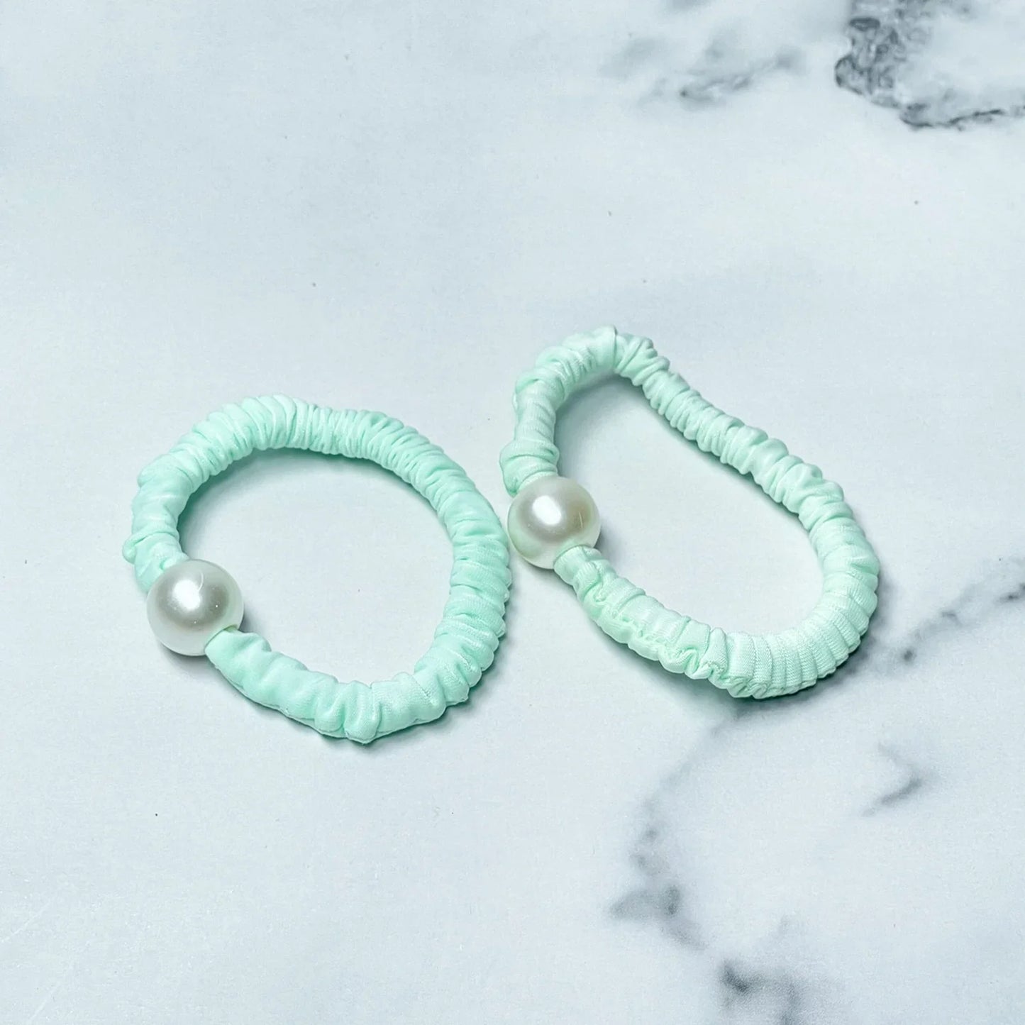 Pastel hair ties with pearl decoration in light mint green on a marble surface