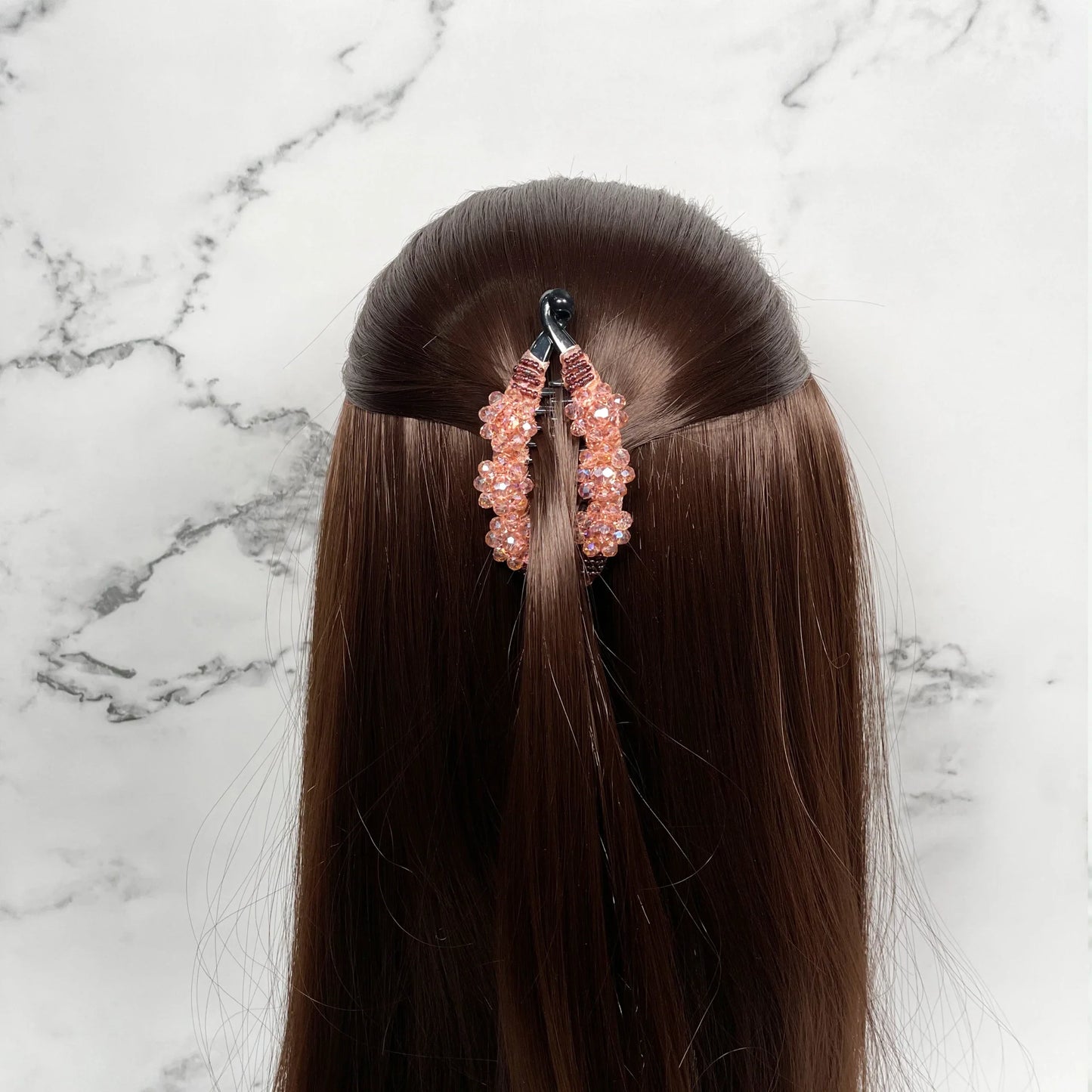 Bella Luxe peach crystal studded banana clip securing brown hair against marble background