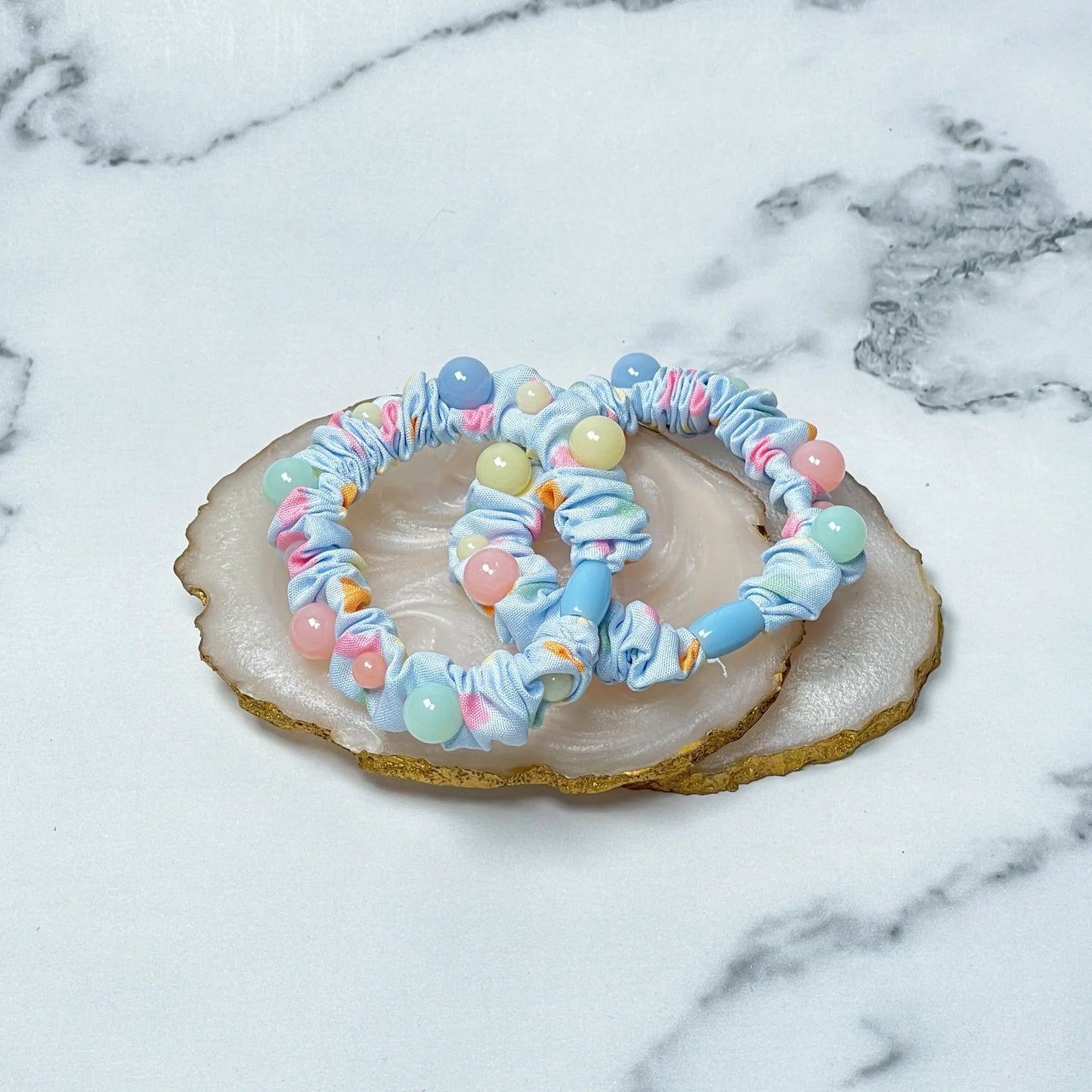 Colorful printed hair ties with pastel beads on agate stone slices on marble surface