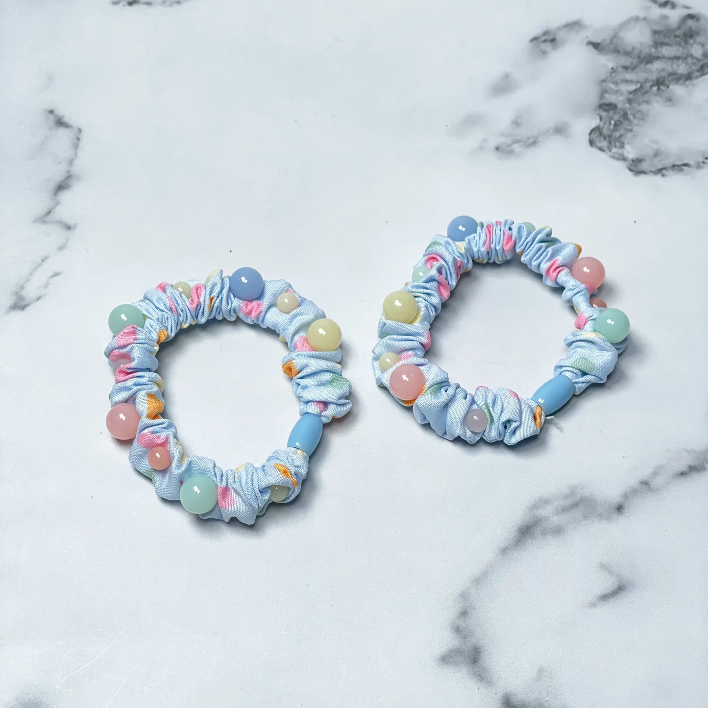 Set of printed hair ties with pastel beads on light blue elastic bands on marble surface