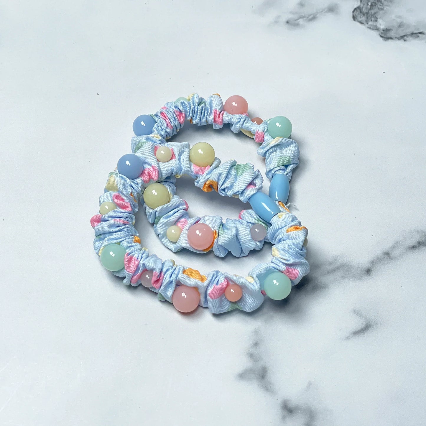 Light blue printed hair ties with colorful beads and vibrant patterns on a white marble surface
