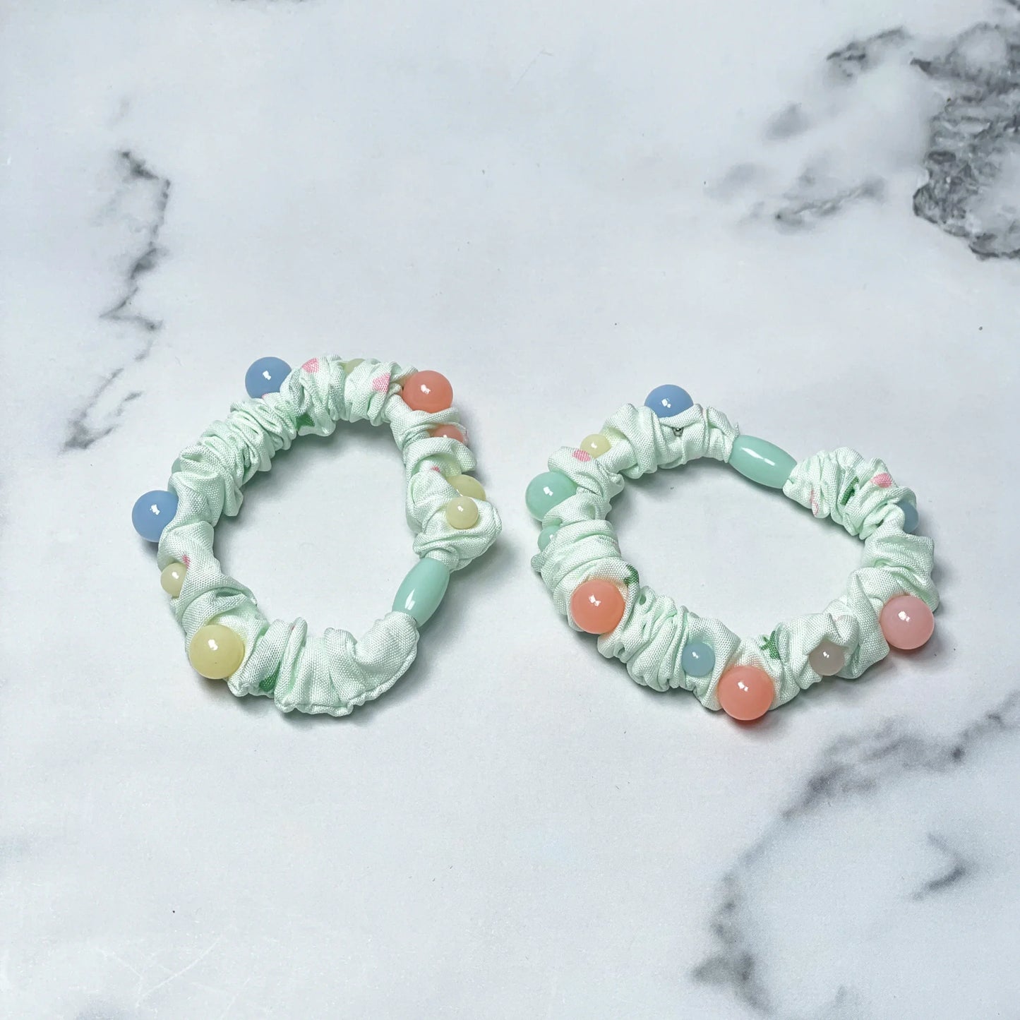 Two white printed hair ties with pastel colored beads on a marble background