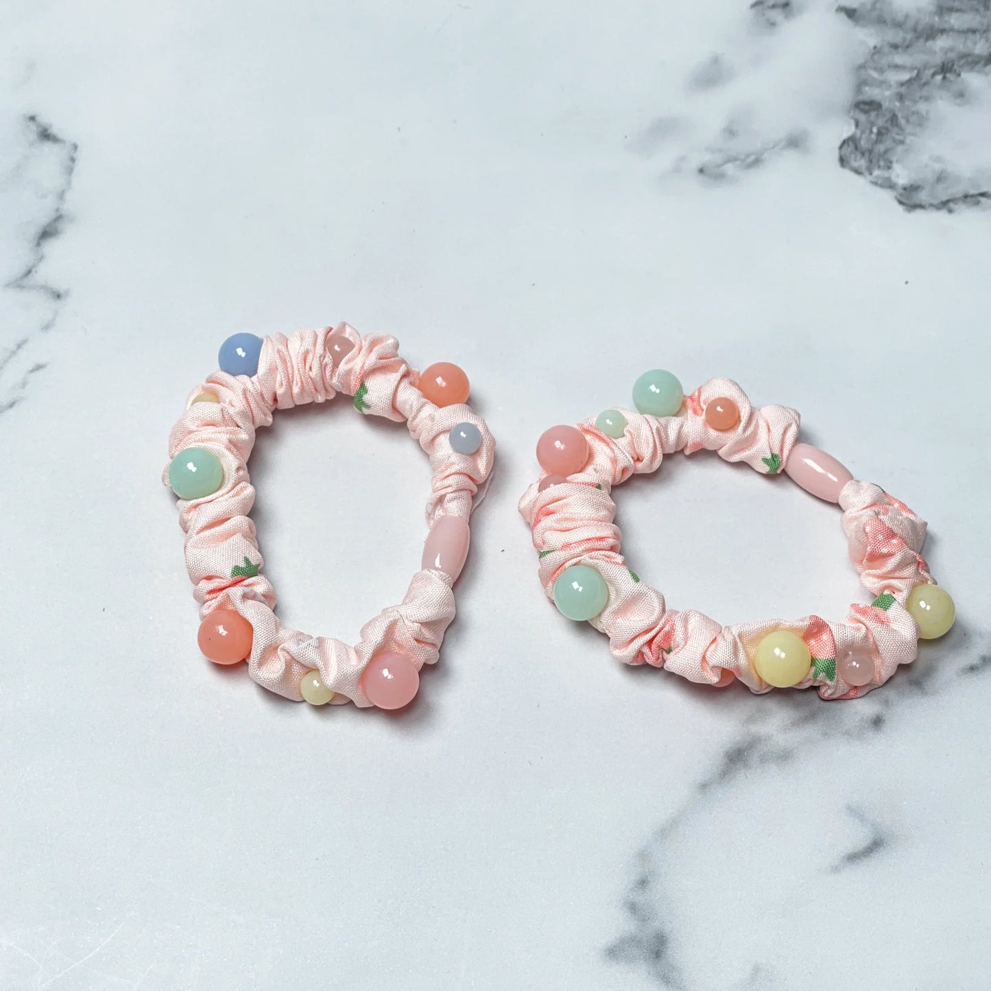 Pink printed hair ties with colorful round beads on a white marble surface