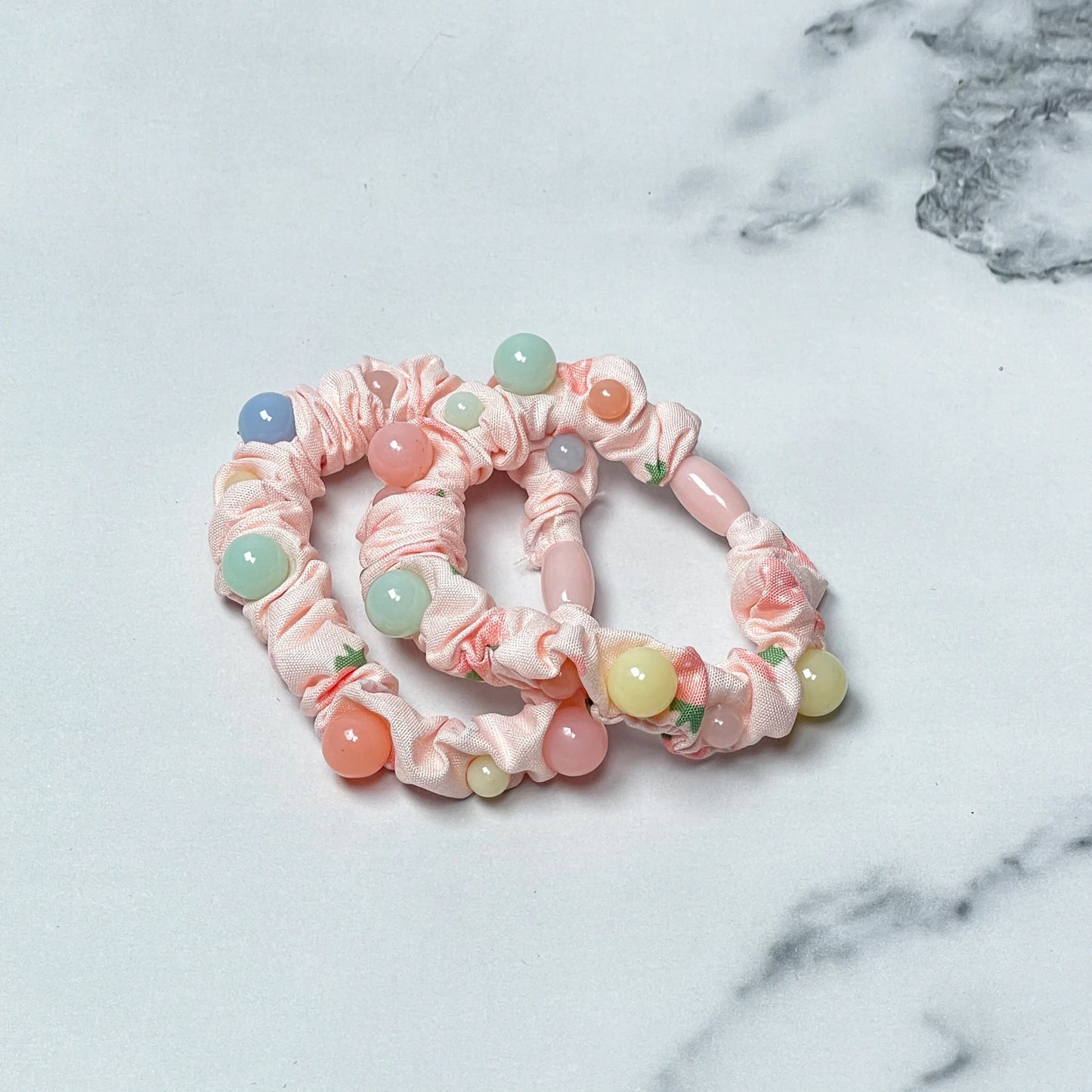 Pink printed hair ties with colorful beads laid on white and gray marble surface