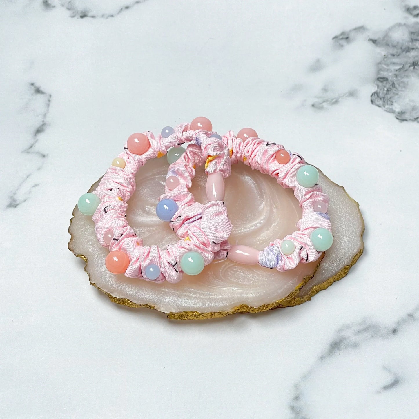 Pink printed hair ties with colorful beads placed on a decorative stone coaster