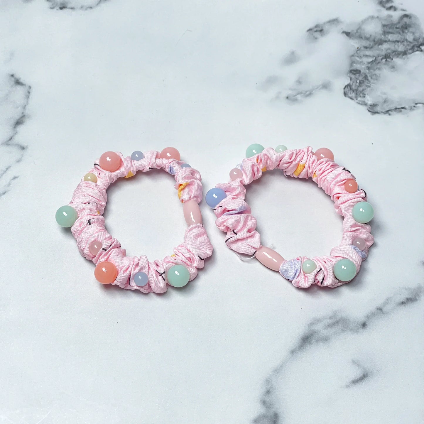 Pink printed hair ties with colorful beads displayed on a white marble surface