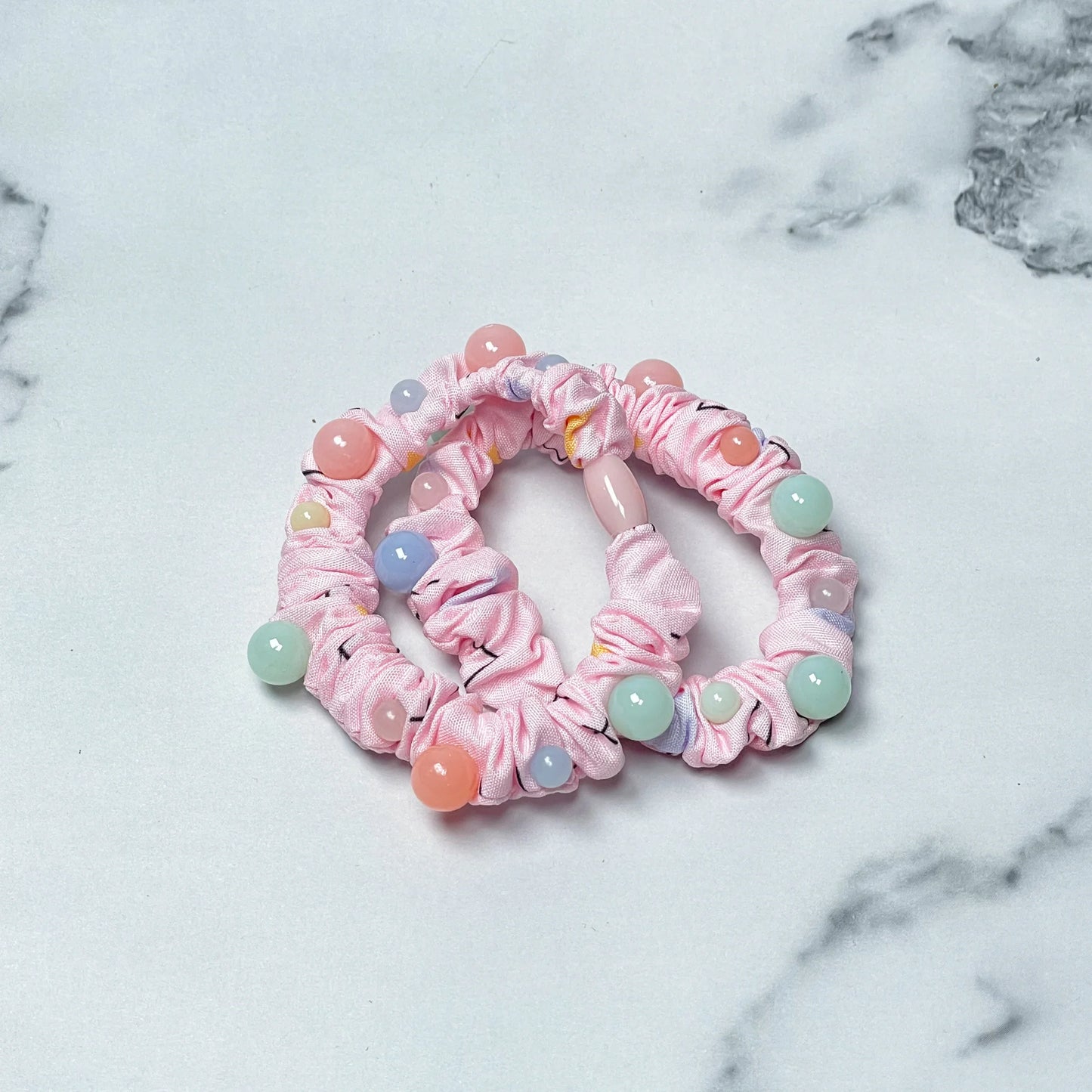 Pink fabric printed hair ties decorated with pastel round beads on a marble background