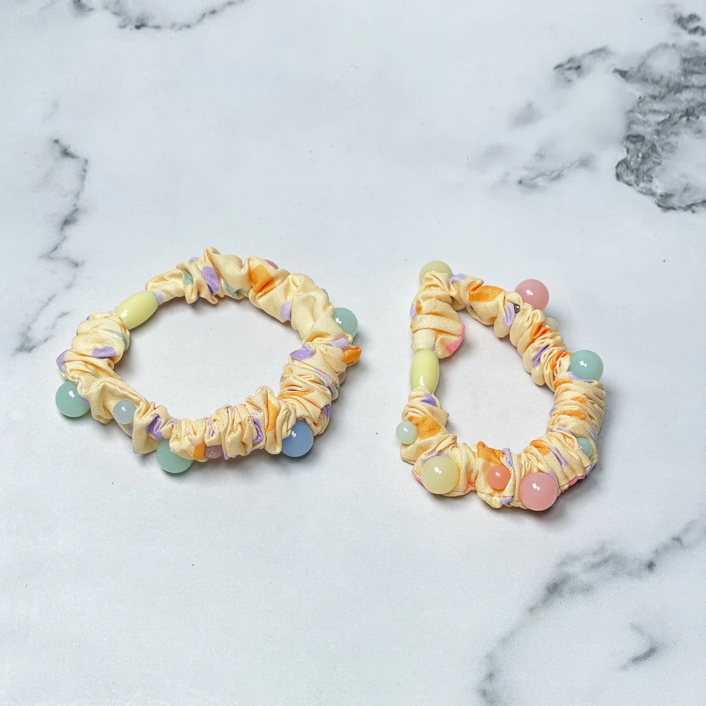 Yellow printed hair ties with colorful beads on white marble background from mydevelopmentstor