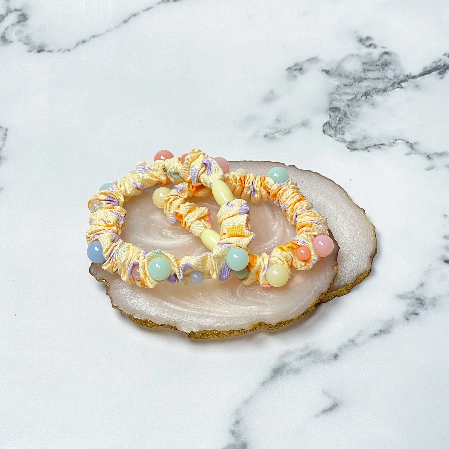 Yellow printed hair ties with pastel beads arranged on a white and gold stone slice