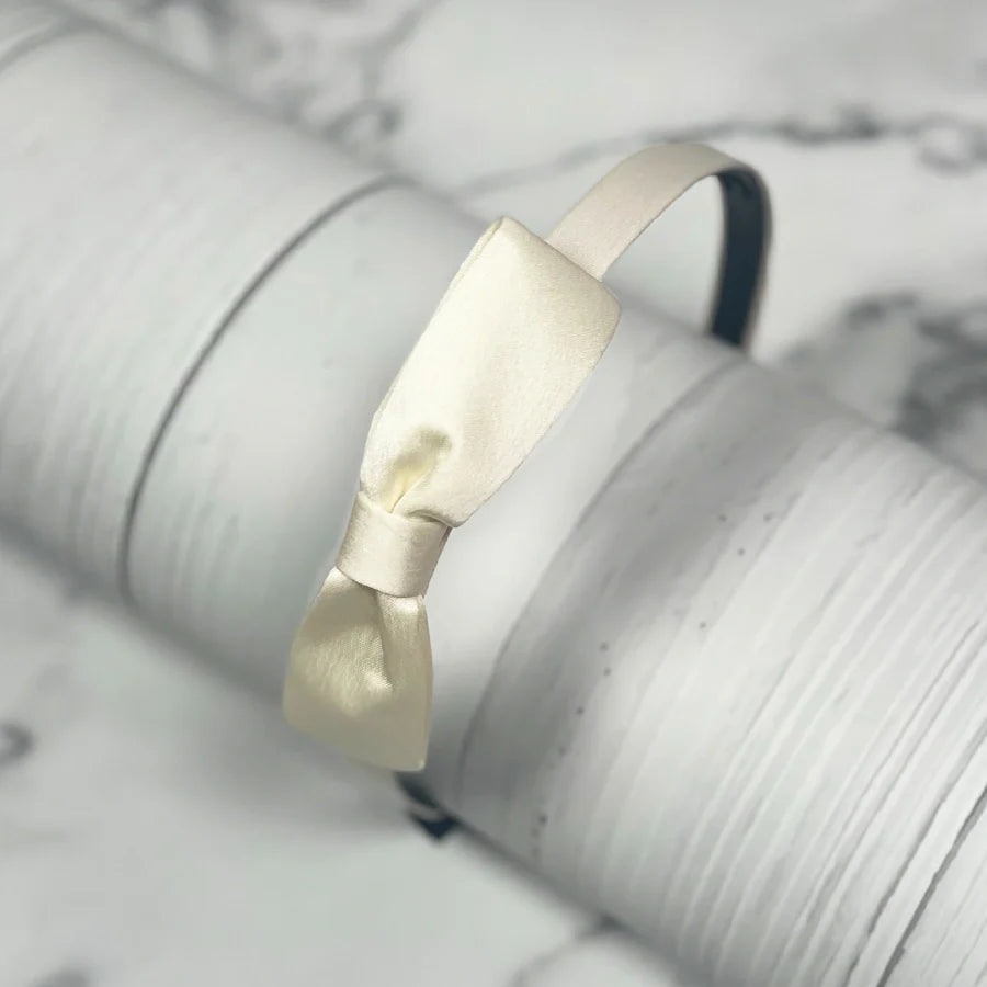 Elegant cream satin bow hairbands displayed on a white textured surface for stylish hair accessories