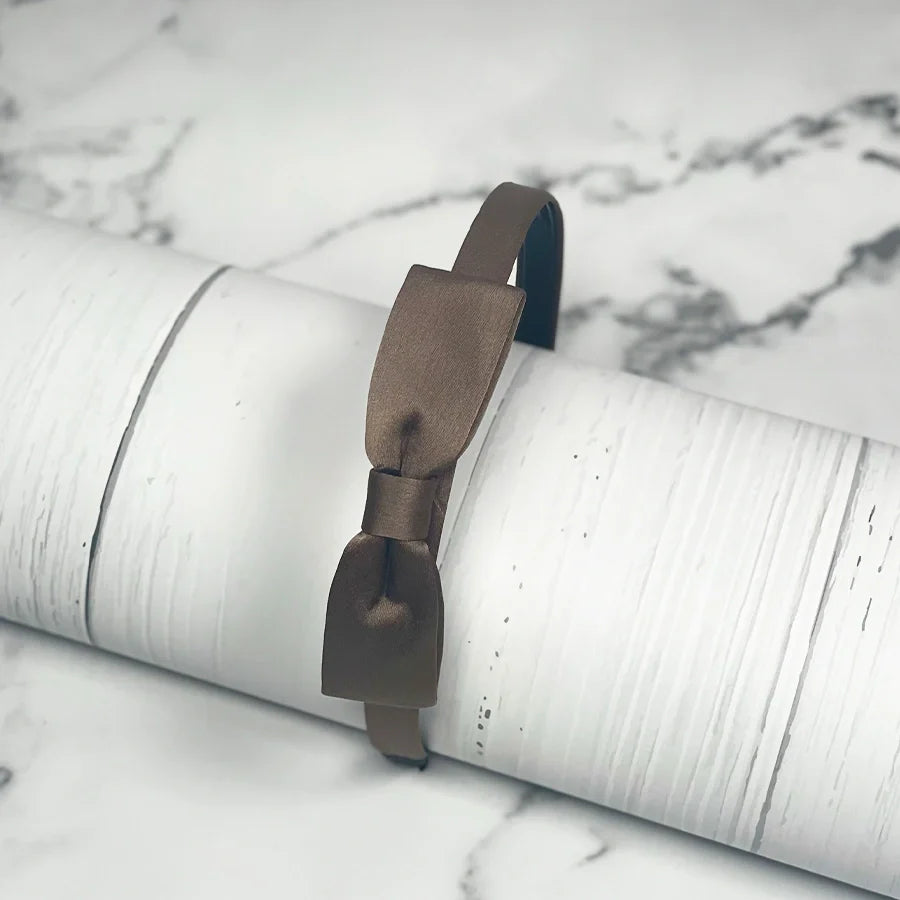Brown satin bow hairbands with a sleek satin finish displayed on a white textured surface