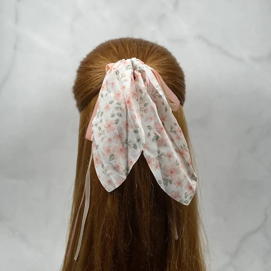 Floral scrunchies with ribbon for women tied in long red hair on gray background