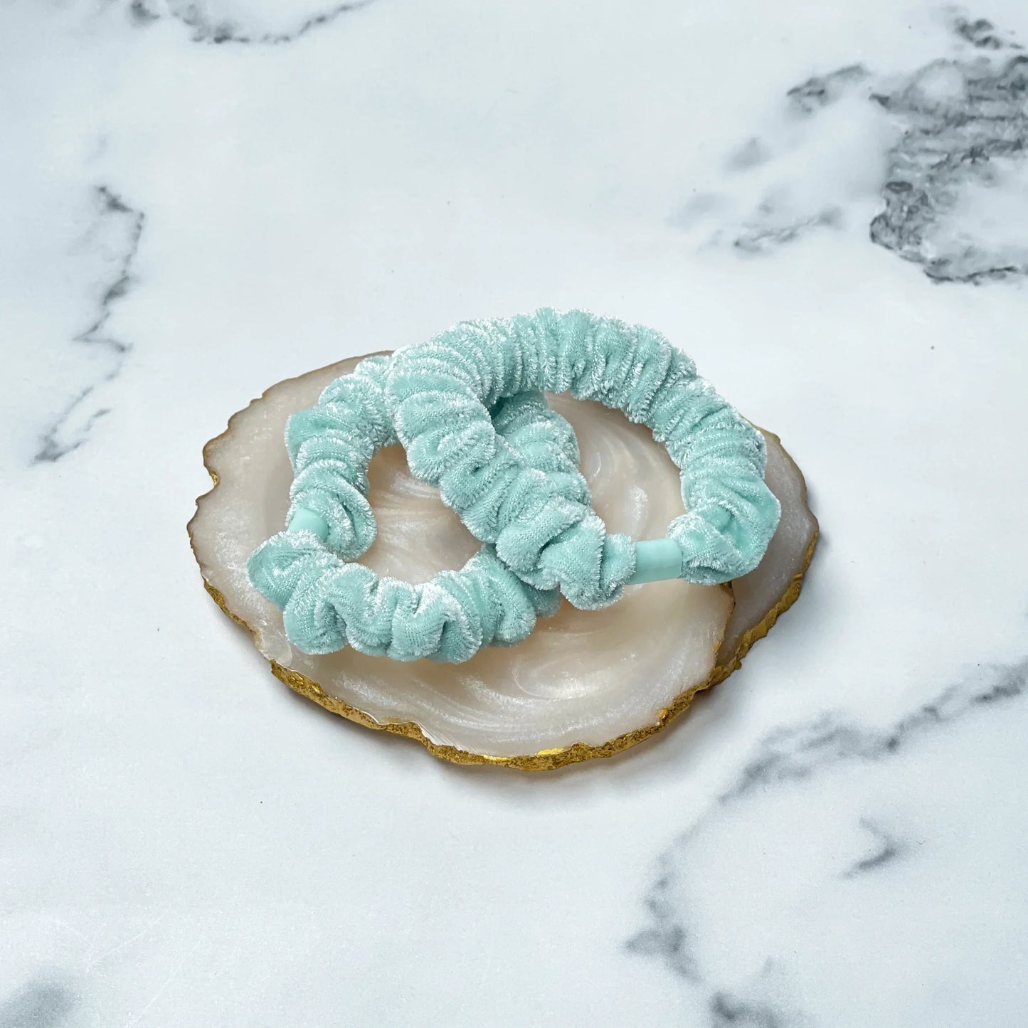 Two light blue shiny velvet hair ties on a white and gold decorative stone plate