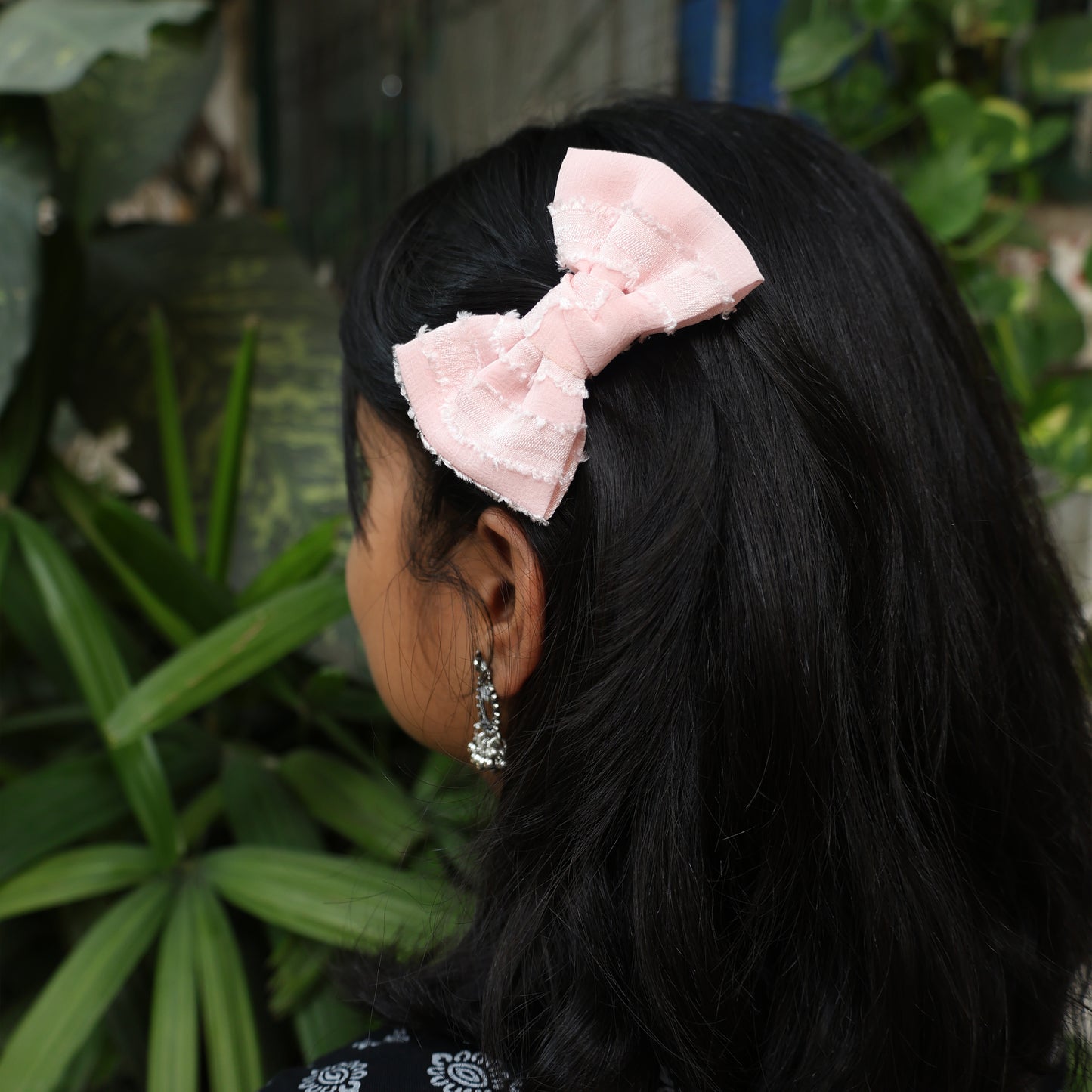 Bella Luxe Small Georgette Bow Clips in soft pink worn on black hair with green foliage background