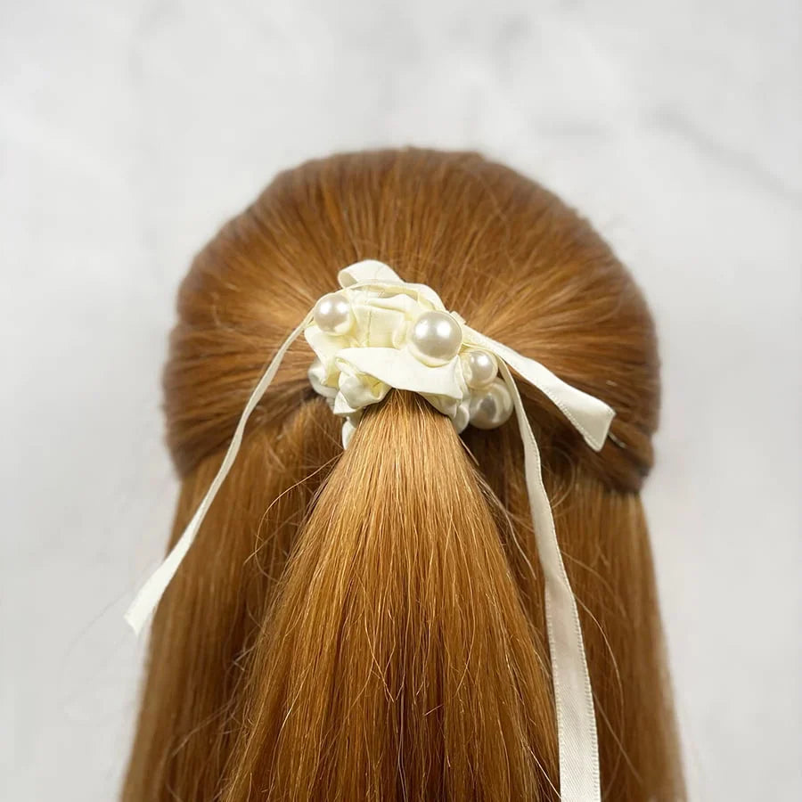Soft cloth hair scrunchie in cream color with pearl accents tied on red hair ponytail