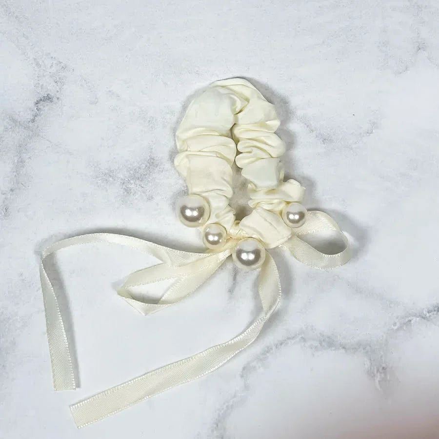 Cream soft cloth hair scrunchie with decorative pearls and long ribbon ties on marble background