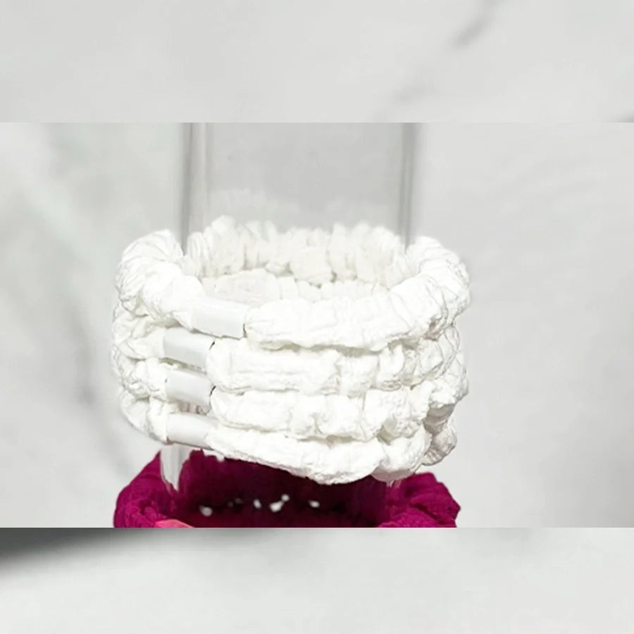 Set of white soft cloth hair ties stacked on a clear glass container with a magenta hair tie below