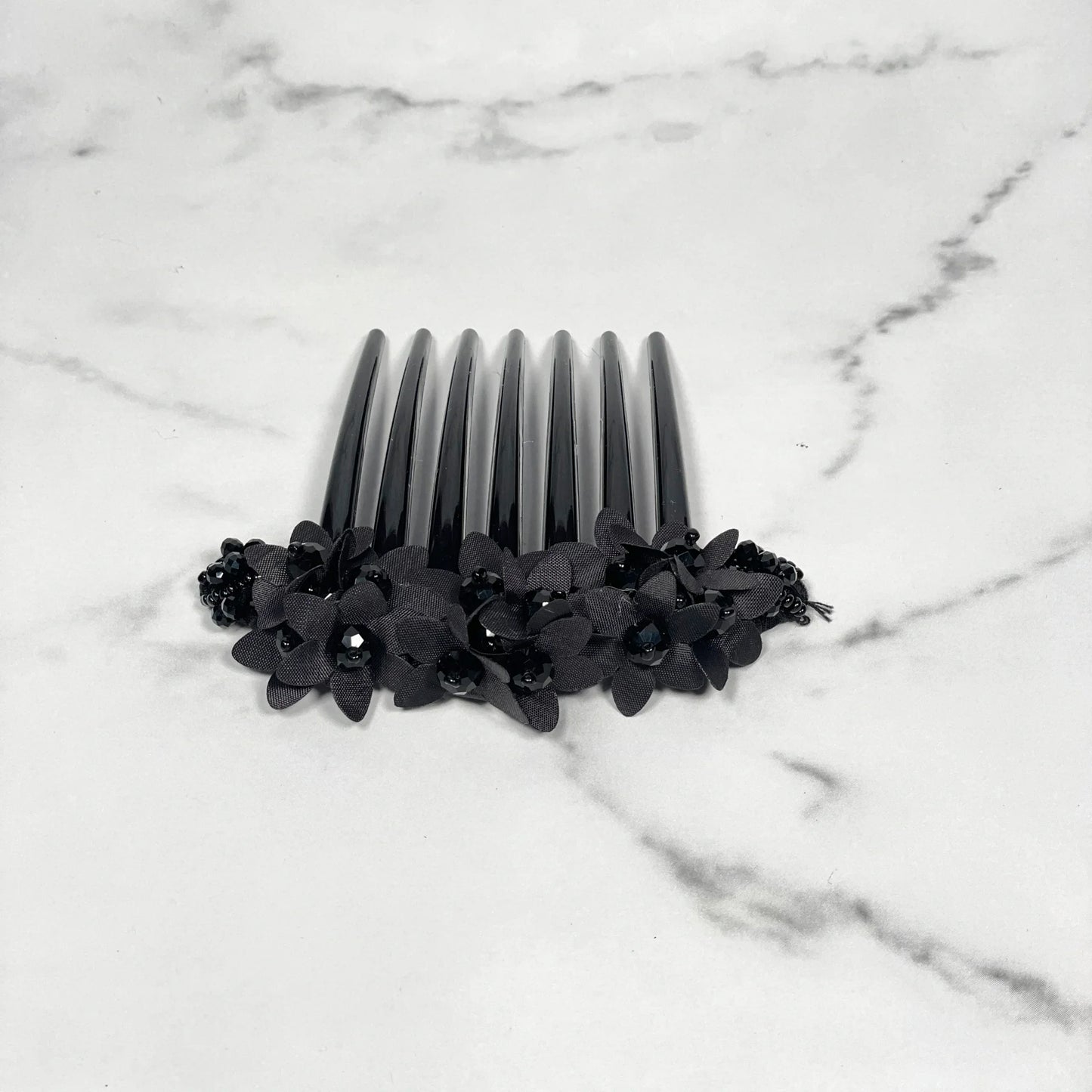 Black studded hair bun comb decorated with black flower accents on a marble background