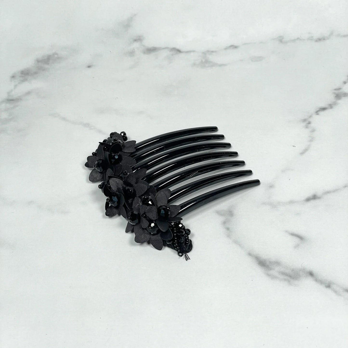 Black studded hair bun comb with floral and bead embellishments on marble surface