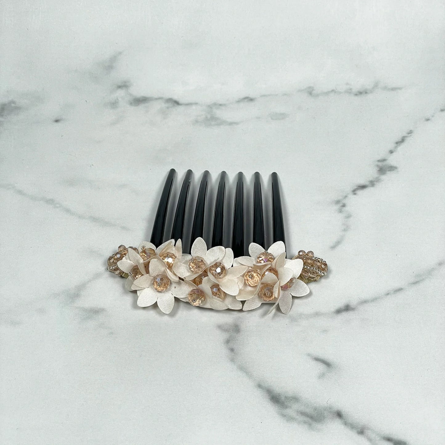 Black studded hair bun comb with white flower decorations and clear gem accents on marble background